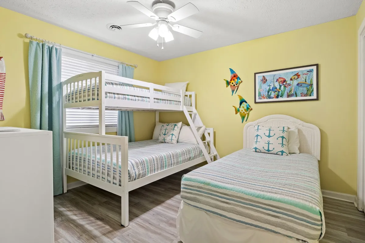 A cheerful second bedroom featuring a bunk bed, an additional single bed, and nautical-themed bedding adorned with colorful fish decorations. The room is well-lit and designed to be playful, making it suitable for children or multiple guests.