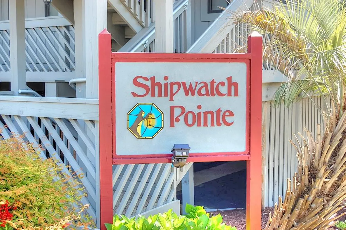 An inviting exterior view of the Shipwatch Pointe sign, surrounded by lush greenery and a staircase leading to the building. The image hints at the property’s proximity to attractions and the pleasant ambiance of the surrounding area.