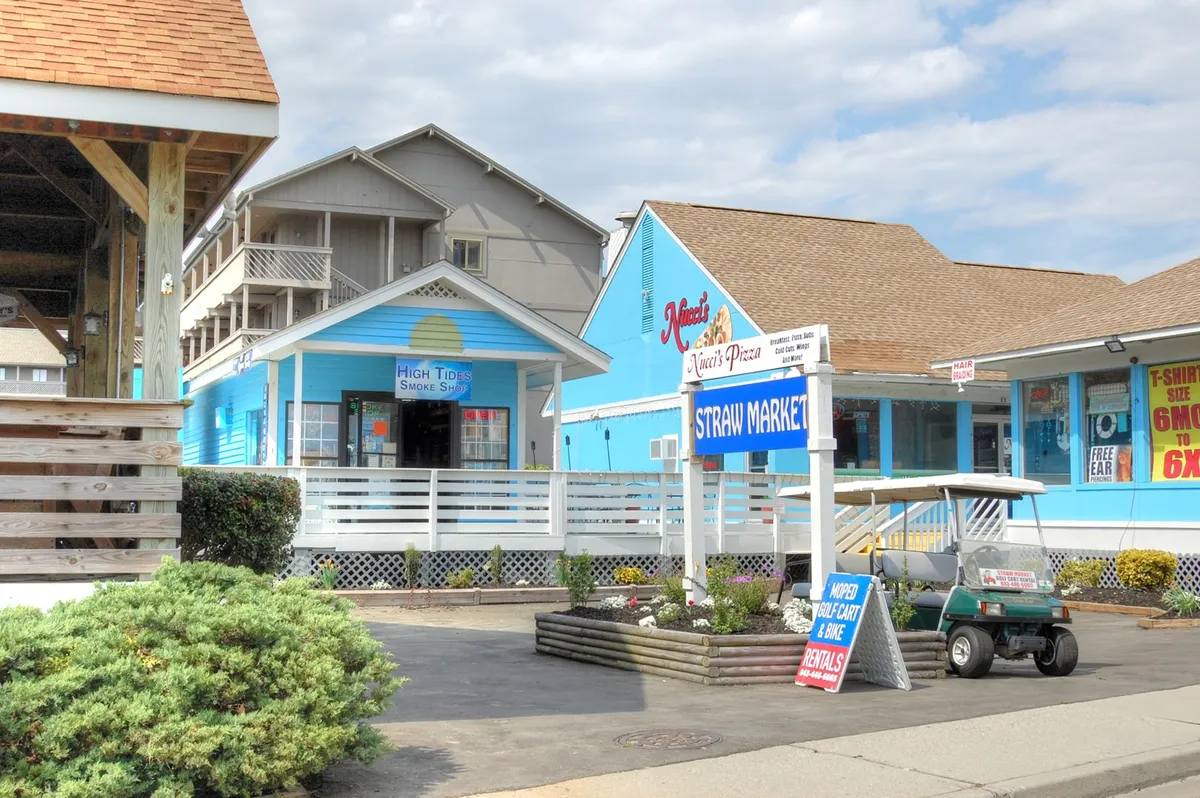 This cheerful exterior shot displays a row of colorful buildings with prominent storefront signs and a golf cart ready for rentals. It showcases a vibrant shopping and dining area, with the inviting colors and sunny weather suggesting a welcoming place for all types of visitors.