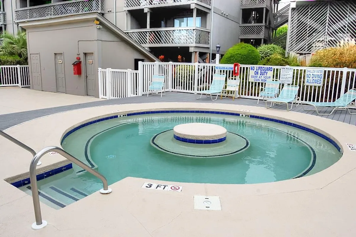 A hot tub surrounded by a privacy fence, lush greenery, and several lounge chairs. The space feels serene yet sociable, perfect for relaxing after a day of adventures or mingling with other guests.
