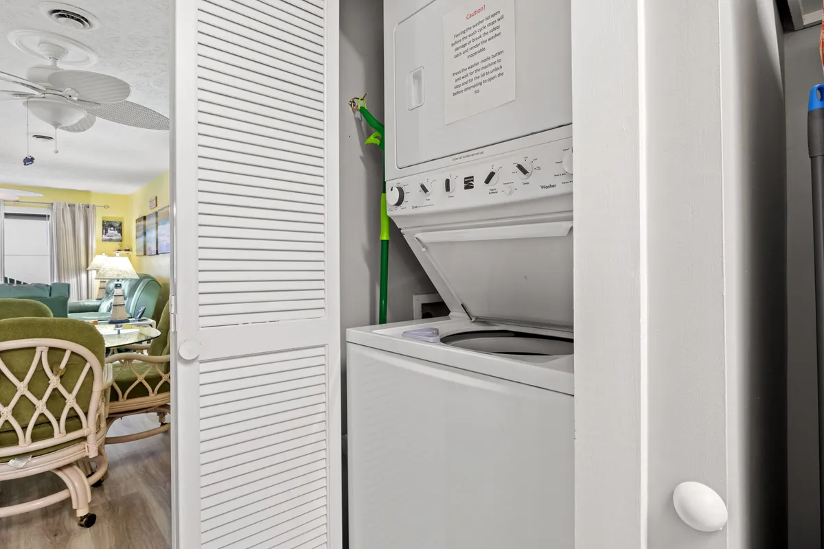 A practical laundry area with a washer and dryer unit, green cleaning supplies, and an open door. The space is clean and functional, designed for easy multitasking and household routines.