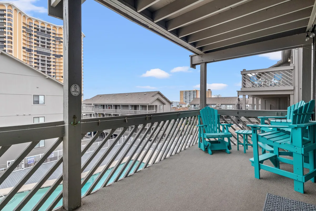 A private balcony is outfitted with turquoise Adirondack chairs and offers views of surrounding buildings. The scene is laid-back, with space for relaxing alone or sharing morning coffee or evening drinks with loved ones.